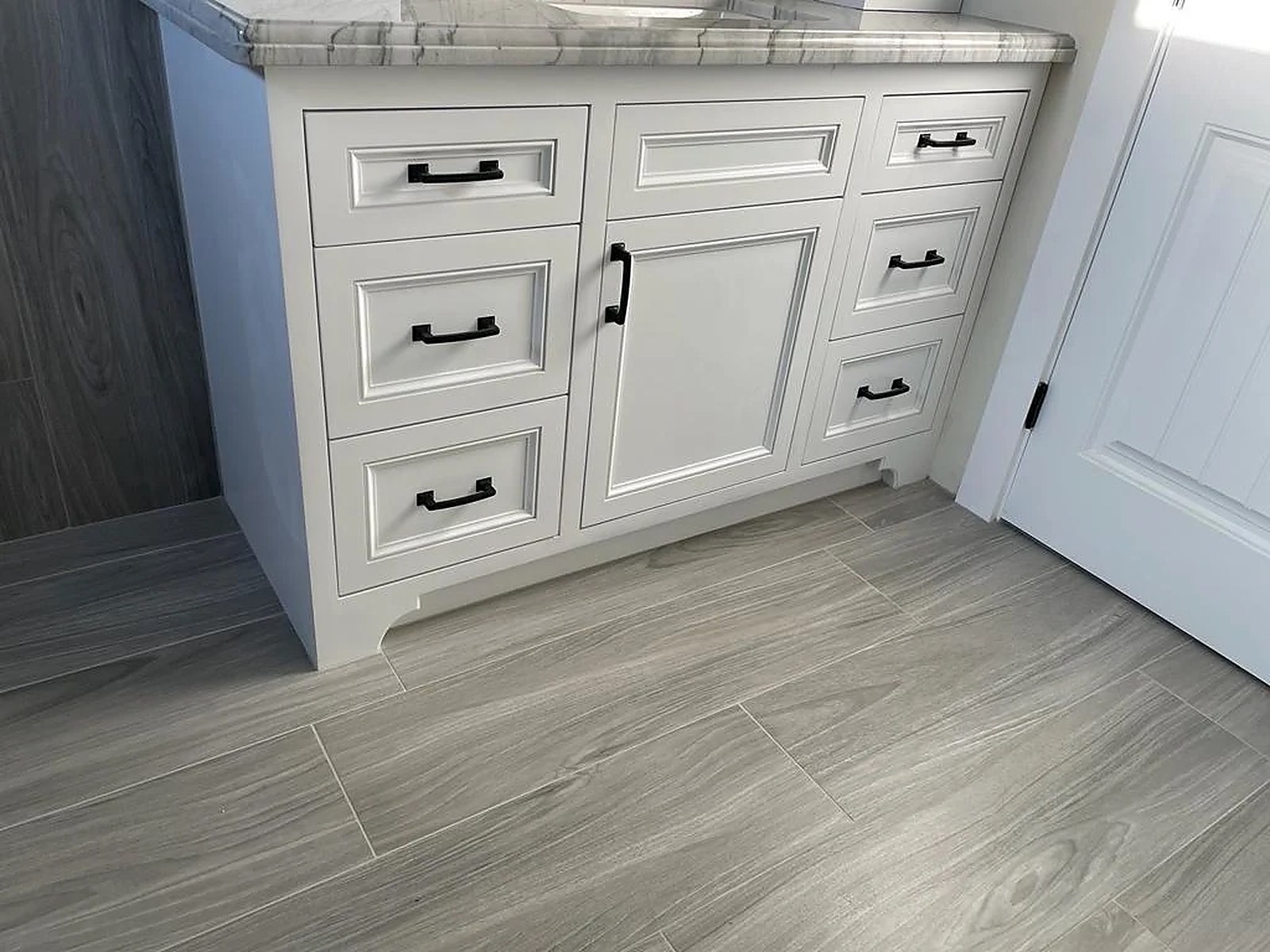 White shaker vanity with marble counter and wood-tile wall