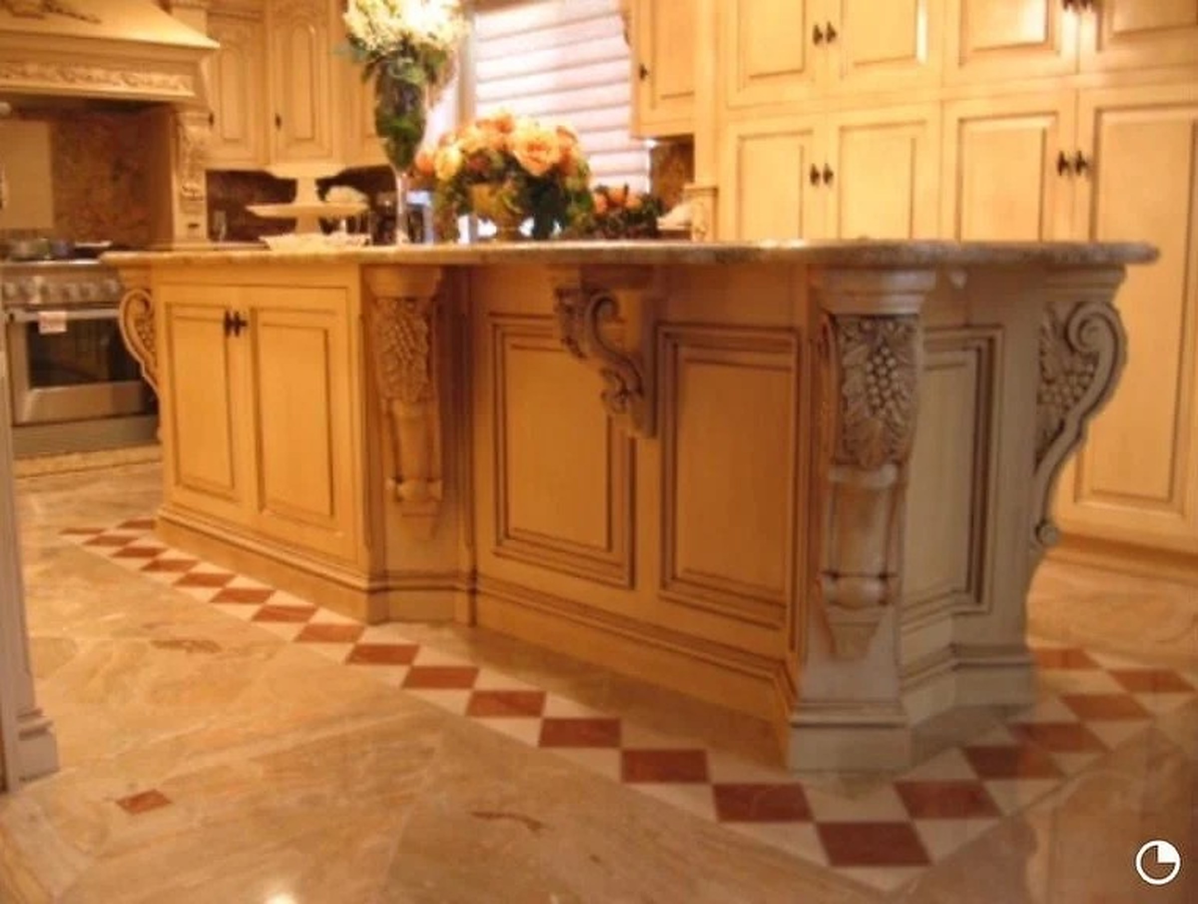 Cream glazed kitchen with a large island carried on hand-carved corbels, raised-panel doors and a checkered stone floor. Custom cabinetry by Premier Cabinets Innovations, Sacramento, California.