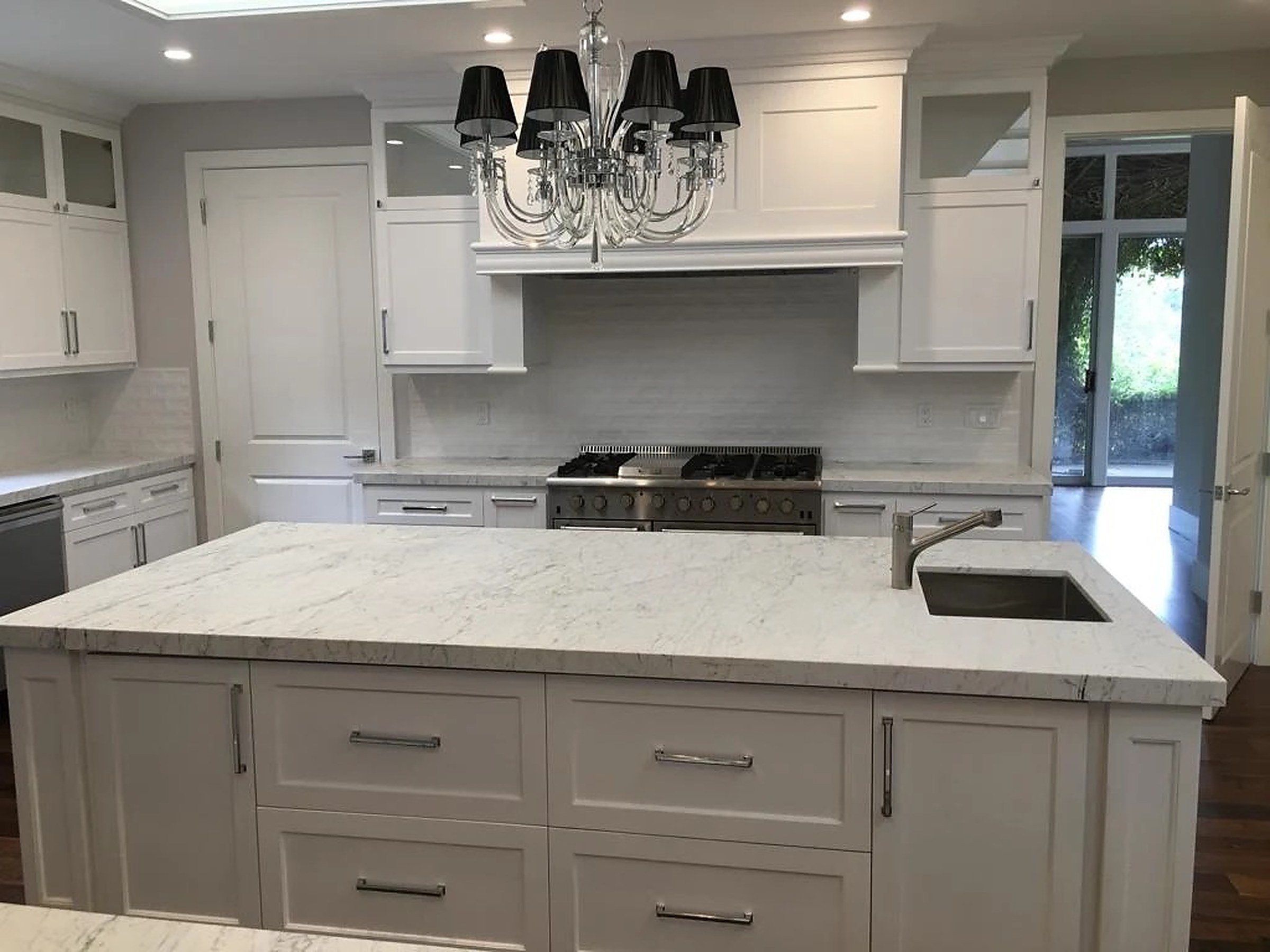 White kitchen with veined marble island and crystal chandelier over pro range