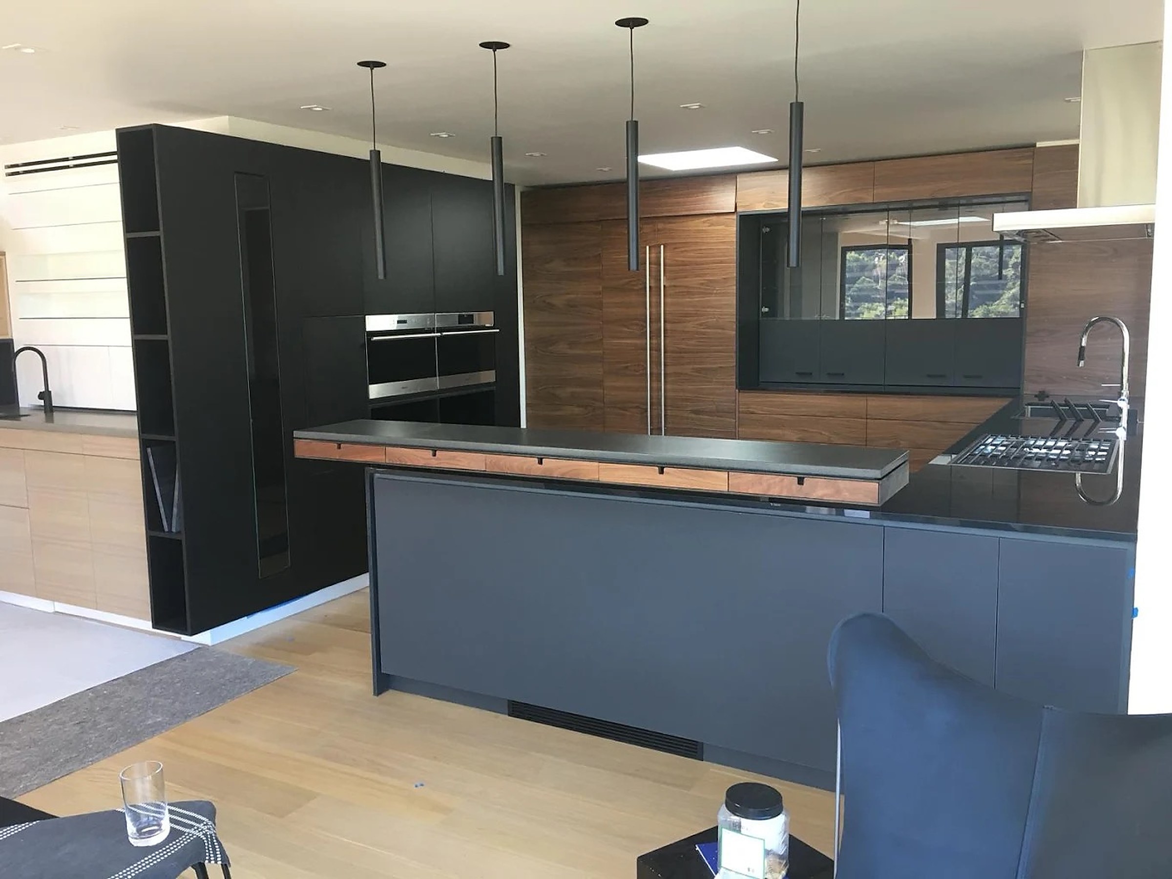 Matte-black slab kitchen with walnut wall and honed stone counter