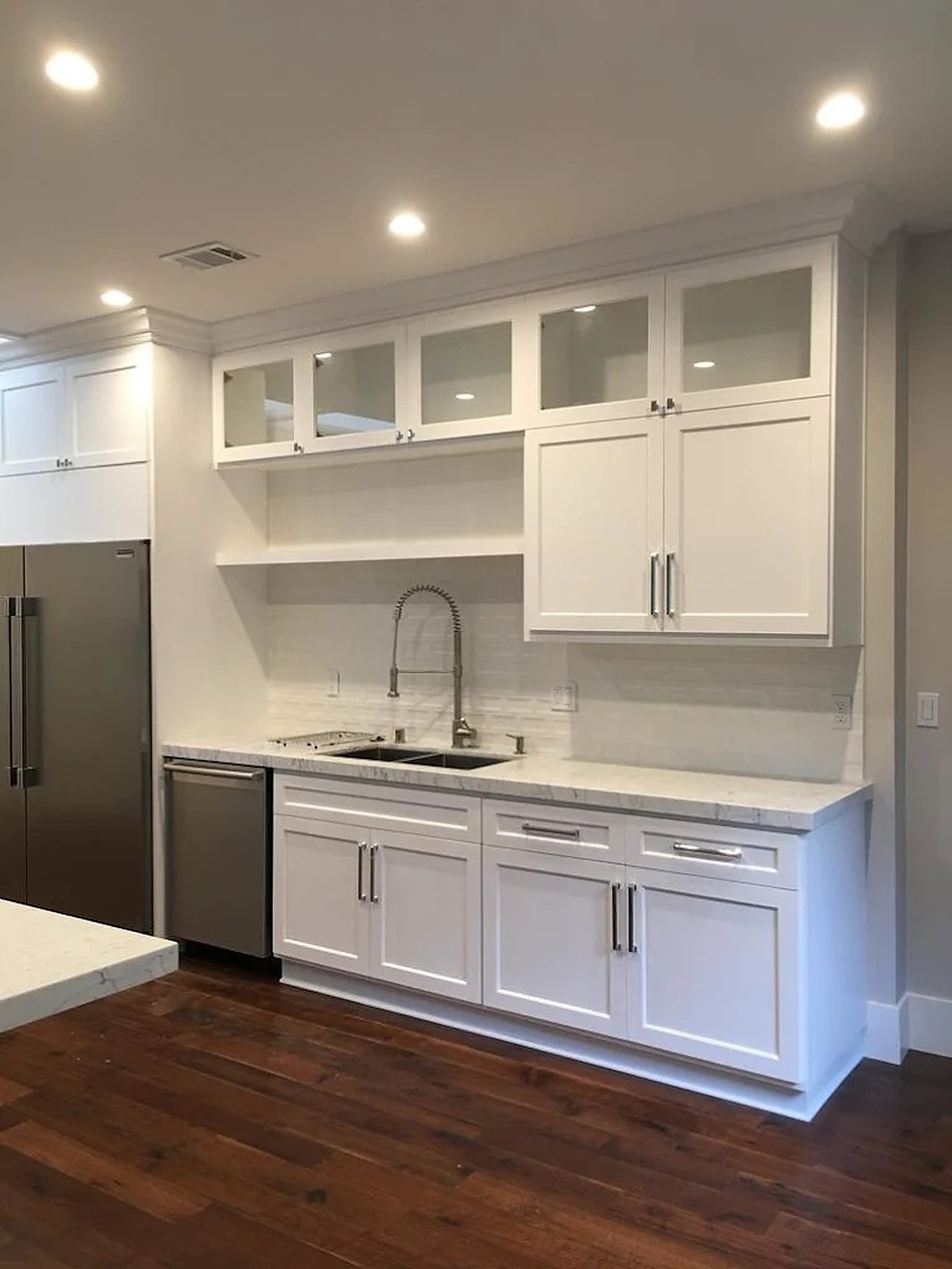 White shaker kitchen with glass-front upper display cabinets, quartz counters and dark hardwood floors. Custom cabinetry by Premier Cabinets Innovations, Sacramento, California.