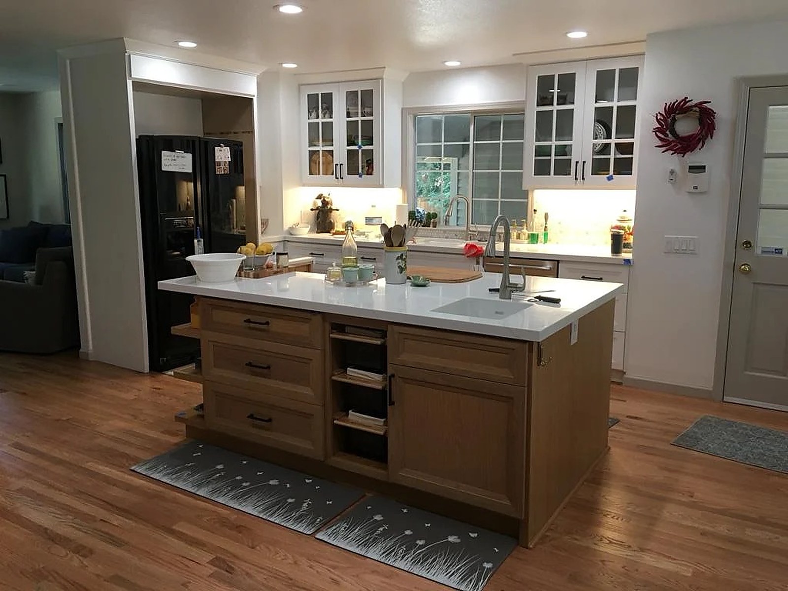 Kitchen with a stained wood island carrying open end shelving, white glass-front upper cabinets and quartz counters. Custom cabinetry by Premier Cabinets Innovations, Sacramento, California.